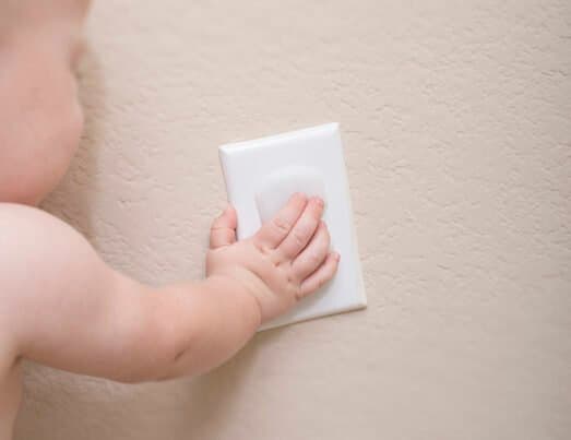 Baby trying to pull off a plastic outlet cover.