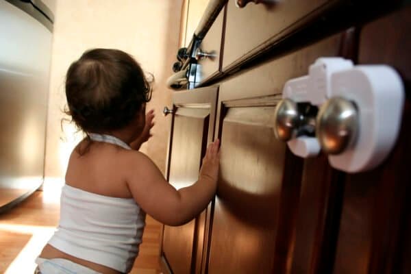 Baby walking next to kitchen cupboards with baby locks installed.