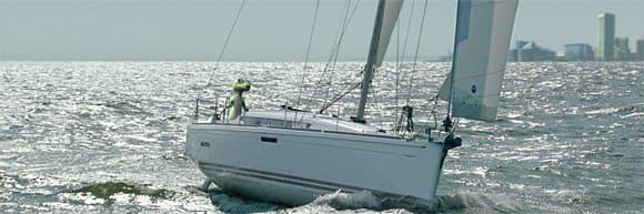 The GEICO Gecko steering a sailboat on open water.