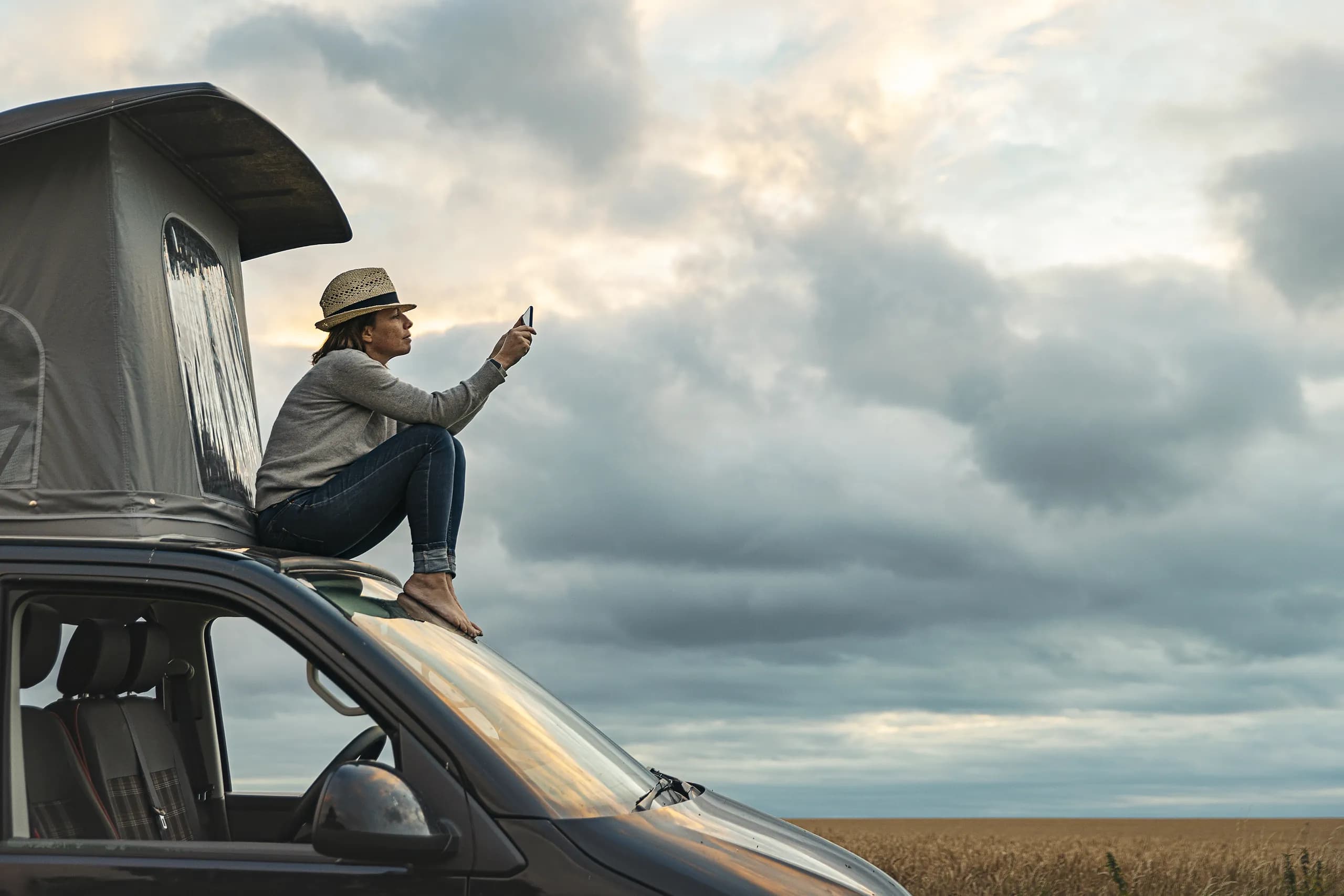 Person sitting on their RV in a field.