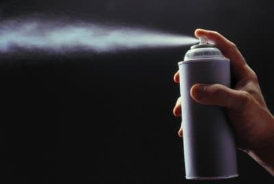 Person spraying an aerosol spray can in front of a black background.
