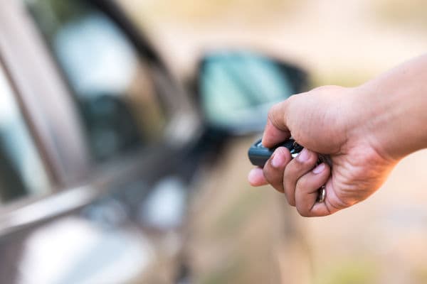 An image of a hand with a key fob near a parked car