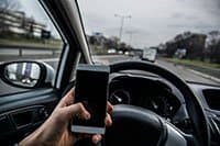 The driver of a car holding up their phone while driving.